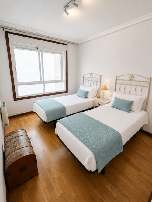 Habitación doble en hotel Holibai de Baiona con dos camas, detalles en azul verdoso y suelo de madera
