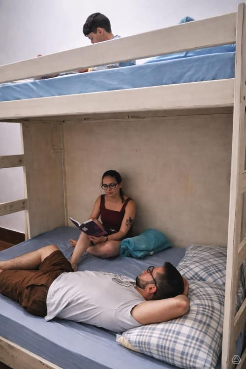 Três hóspedes em uma cama superposta tripla do quarto dormitório do Rio Vibes Hostel no Rio de Janeiro com roupa de cama azul e ar condicionado