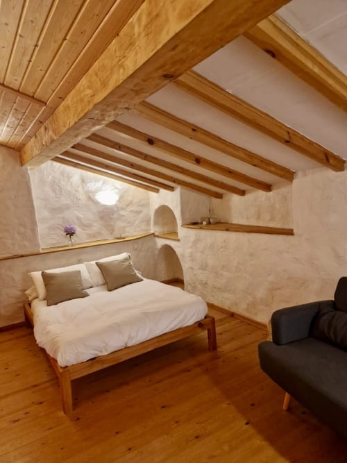 Dormitorio rústico en Casa Aldea L'Ayalga con vigas de madera expuestas, paredes encaladas, cama de madera con sábanas blancas y