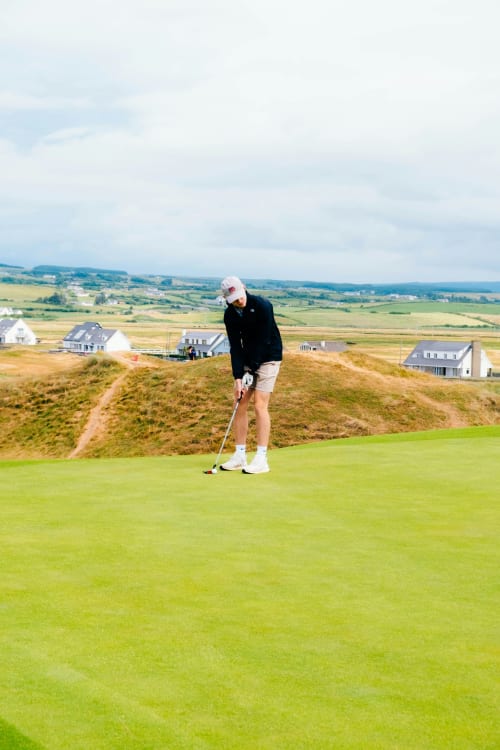 Golfer putting on scenic coastal green at Bucket & Spade, Co. Clare with countryside views
