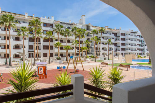 Complejo de apartamentos en San Pedro del Pinatar con zona de juegos, piscina y palmeras en el patio