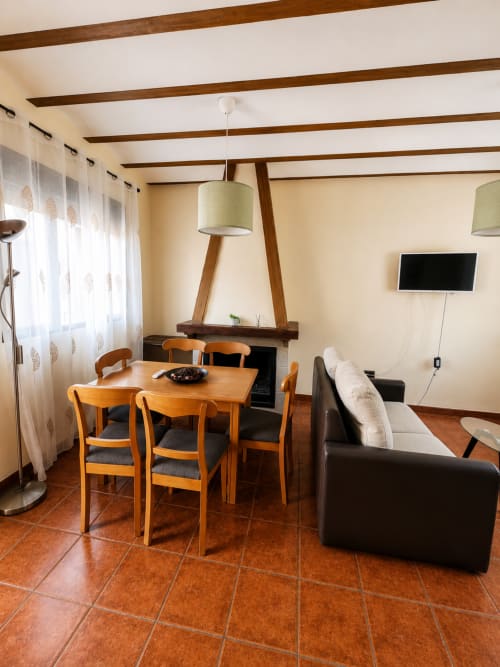 Salón moderno con vigas de madera, comedor, sofá negro, chimenea y TV en villa Finca El Arroyo de Alcaraz