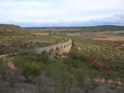 Histórico viaducto de piedra que cruza el valle verde de Alcaraz con molinos eólicos visibles en las colinas lejanas