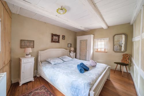 Cozy bedroom at Chez Ambre cottage in Eguisheim with white bed, beige walls, wooden beams, and classic decor.