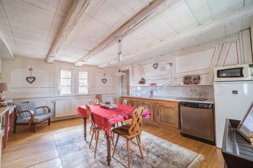 Bright cottage kitchen and dining area in Eguisheim with wooden beams, heart decorations, and rustic dining table set with