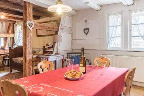 Dining room at Chez Ambre cottage in Eguisheim with red tablecloth, wooden chairs, champagne bottle, and rustic Alsatian