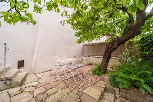 Charming outdoor patio at Chez Ambre cottage in Eguisheim with white chairs under a leafy tree and stone courtyard