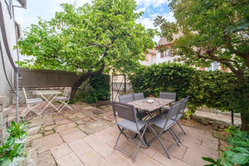 Secluded courtyard at Chez Jade cottage in Eguisheim with dining table, mature trees, and ivy-covered stone walls