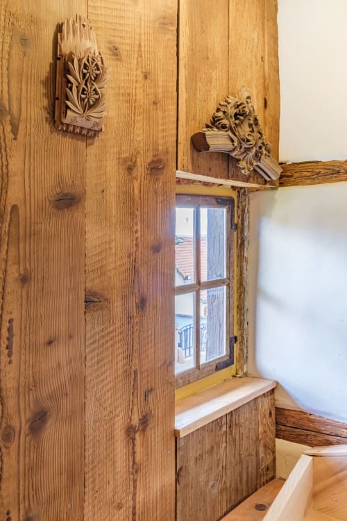 Rustic wooden interior at Chez Ambre cottage in Eguisheim with carved wall details and window overlooking rooftops