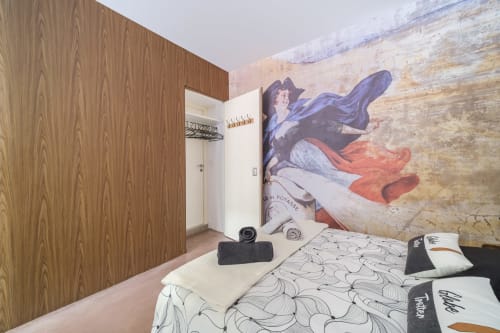 Modern bedroom at Les Ambrades in Colmar featuring wood paneling, patterned bedding, and Renaissance mural artwork