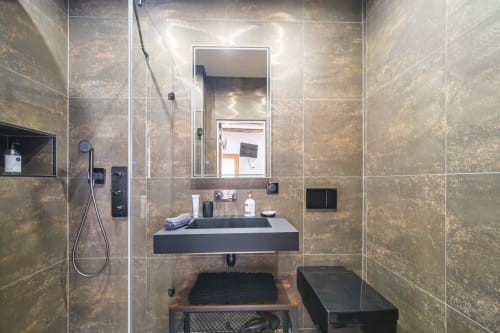 Modern bathroom at Les Ambrades, Colmar with bronze-tiled walls, floating sink, mirror, and contemporary fixtures