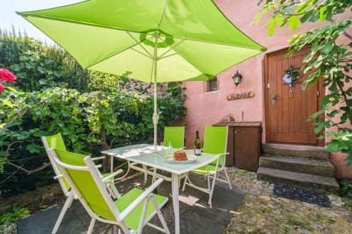 Charming patio at Les Ambrades villa in Eguisheim with lime green umbrella, chairs, and table overlooking lush gardens