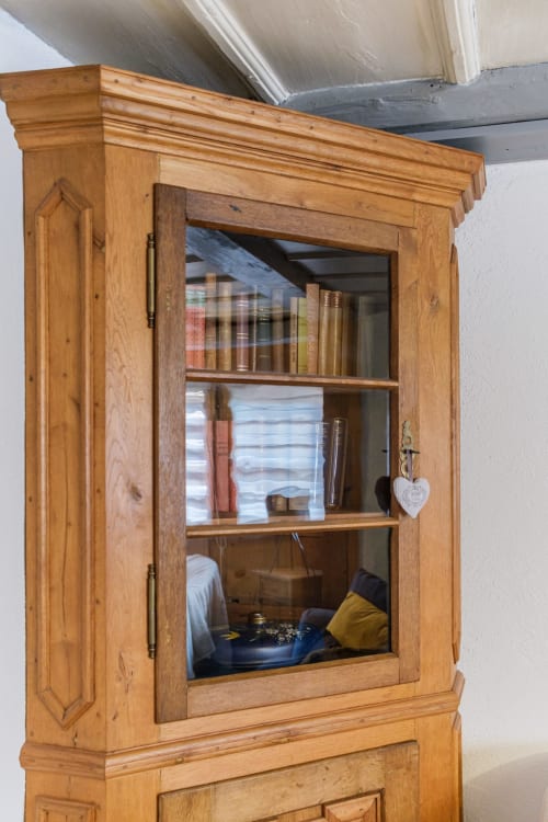 Wooden glass cabinet with shelves displaying books and decorative items at Les Ambrades villa in Eguisheim