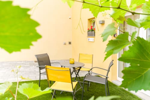 Gemütliche Außenterrasse des Cottage Les Ambrades in Kaysersberg mit gelben Stühlen, Tisch und Kletterpflanzen an cremefarbener Wand.