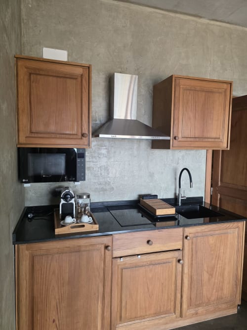 Pequeña cocina moderna en suite Les Terrasses con muebles de madera, encimera negra y electrodomésticos de acero inoxidable