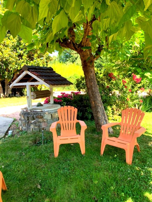 Deux chaises Adirondack orange sur pelouse verte sous un grand arbre au jardin du Clos Bussy à Bellerive-sur-Allier