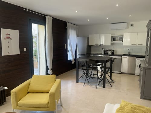 Appartement moderne et ouvert à la Maison Dormoy Marseille avec fauteuil jaune, table noire, cuisine blanche et mobilier sombre