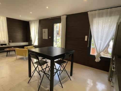 Appartement moderne à la Maison Dormoy à Marseille avec table à manger noire, boiseries sombres, rideaux crème et vue sur la ville