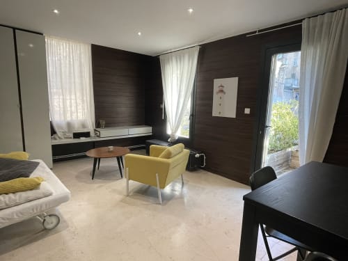 Chambre moderne de l'appartement Maison Dormoy Marseille avec fauteuil jaune, boiseries sombres et accès à la terrasse