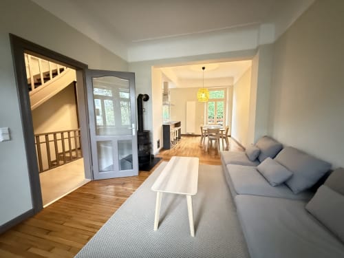 Séjour spacieux et lumineux avec canapé gris, table basse blanche, parquet, accès à la salle à manger et escalier