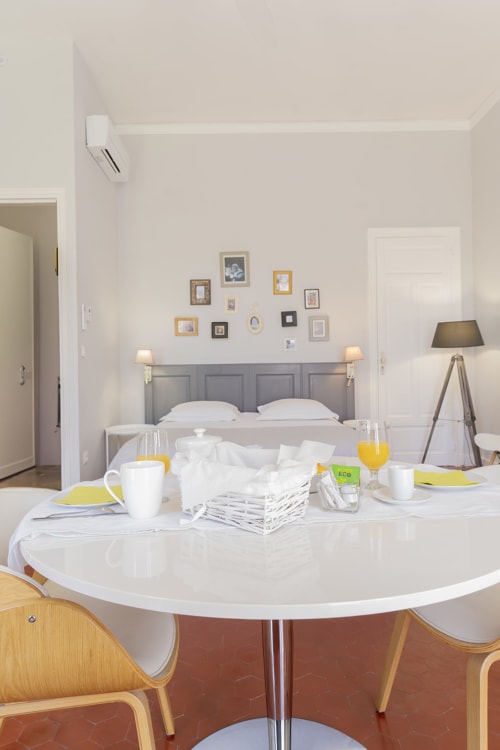 Chambre moderne à la Maison Dormoy à Marseille avec table à manger ronde, lit à tête de lit grise et galerie murale d'art