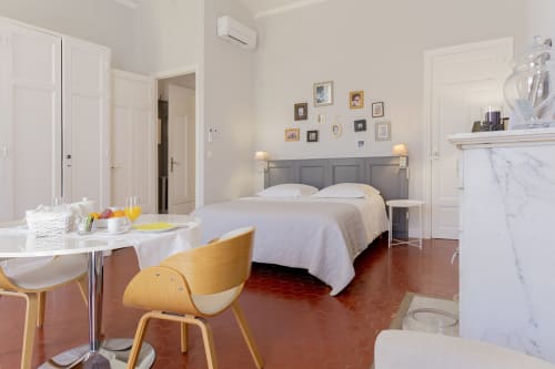 Chambre lumineuse de l'hôtel Maison Dormoy à Marseille avec lit queen-size, tête de lit grise, bureau, carrelage en terre cuite et cheminée en marbre