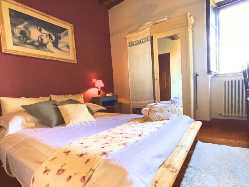 Ampia camera da letto con letto in legno, pareti bordeaux e vista sul castello a Torre Della Chiocciola B&B a Monteriggioni, Siena