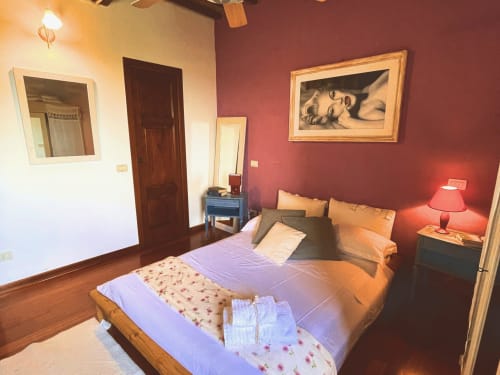 Camera da letto con letto in legno, pareti bordeaux, specchio, scrivania e vista sul castello presso Torre Della Chiocciola B&B a Monteriggioni