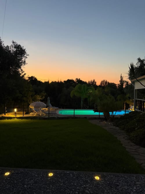 Piscina iluminada ao entardecer com iluminação verde e azul, terraço do bungalô Casa Verde, jardins e árvores circundantes