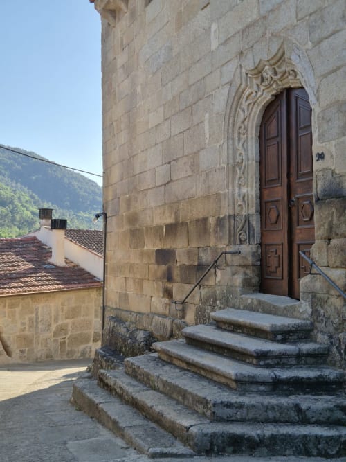 Entrada de piedra de Aldea Rural Pazos De Arenteiro con puerta de madera ornamentada, montañas al fondo, España