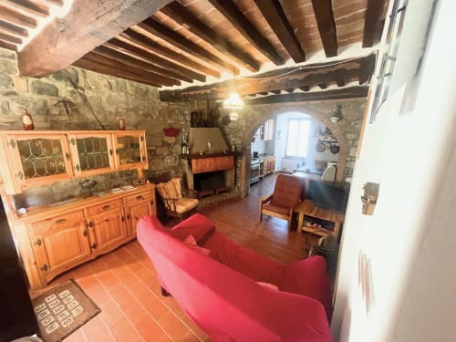 Soggiorno rustico con travi in legno a vista, muri in pietra, divano rosso, arredi in legno e angolo cottura a Torre
