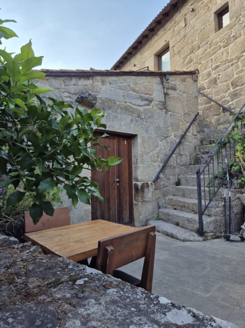 Rústica zona de estar en patio de piedra de Aldea Rural Pazos De Arenteiro con bancos de madera y plantas verdes