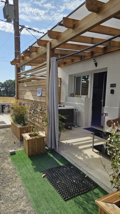 Patio moderne de la Résidence L'Hermitière avec pergola en bois, façade blanche, plantes en pots et vue sur le lac
