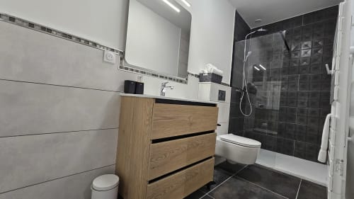 Salle de bain moderne avec meuble vasque en bois, douche carrelée noire et miroir à la Résidence L'Hermitière, vue sur le lac
