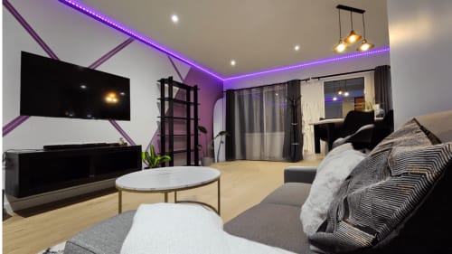 Salon d'appartement moderne avec éclairage LED violet au plafond, TV écran plat, assises grises et table basse blanche