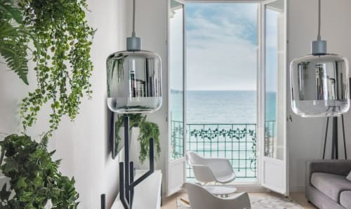 Appartement moderne à Riviera Home avec balcon vue mer, luminaires suspendus, plantes et paysage côtier méditerranéen