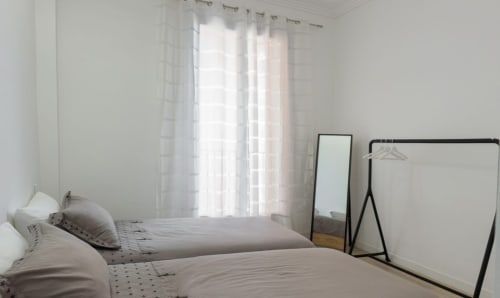 Chambre lumineuse à Riviera Home à Roquebrune-Cap-Martin avec rideaux voilages, lits jumeaux, miroir sur pied et balcon vue mer