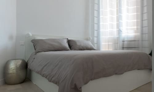 Chambre moderne à Riviera Home avec literie grise, tête de lit blanche, voilages et vue sur la mer de Roquebrune-Cap Martin
