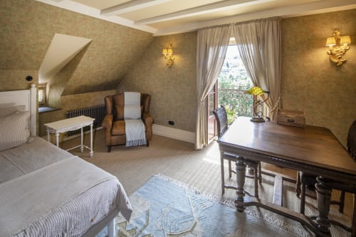 Chambre élégante à La Maison Oubliée avec lits jumeaux, fauteuil, bureau et vue sur le jardin depuis le balcon
