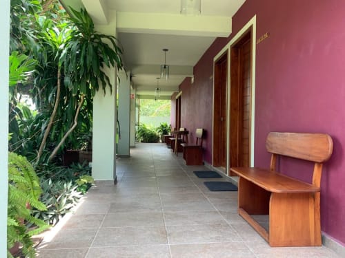 Pasillo del hotel La Morada con paredes púrpura, banco de madera, plantas frondosas y puertas de madera en Monte Gordo