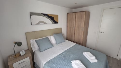 Dormitorio moderno con cama queen, ropa de cama azul, cabecero beige, armario de madera y arte abstracto frente al mar en Oropesa