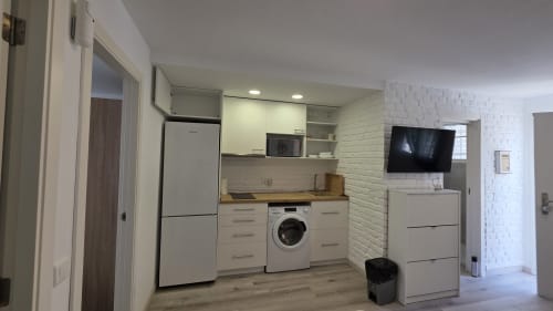 Moderna zona de cocina-sala de estar en cottage Siesta 7 de Monica Socarici, Oropesa. Muebles blancos, electrodomésticos y lavadora