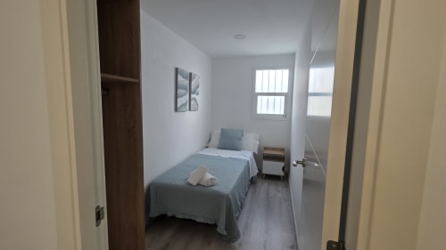 Dormitorio luminoso en la casita de Benicàssim con cama individual, mesilla de noche, ventanas, paredes blancas y suelo de madera