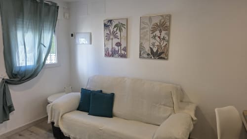 Salón luminoso de la casa rural de Benicàssim con sofá crema, arte botánico decorativo y vista al jardín a través de ventana con cortinas