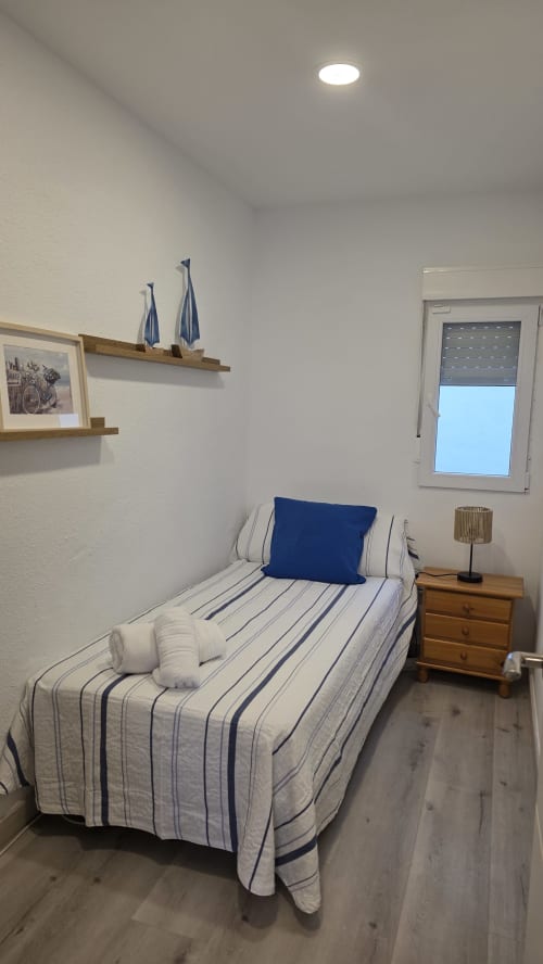 Acogedora habitación en el cottage MONICA SOCARICI, Benicàssim con ropa de cama a rayas, mesita de noche de madera y vistas al jardín