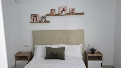 Dormitorio moderno en casita de Benicàssim con cabecero crema, ropa de cama blanca, almohada oliva, mesitas de noche de madera y decoración