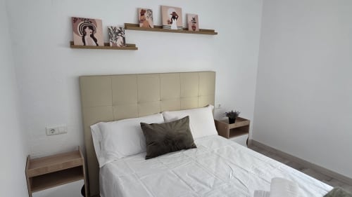 Dormitorio moderno con cabecero beige, ropa de cama blanca, mesitas de noche de madera y estantes flotantes en el bungalow MONICA SOCARICI