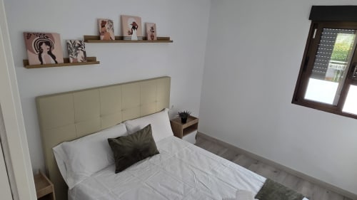 Dormitorio moderno en casa rural de Benicàssim con cabecero crema, ropa de cama blanca, estantes de madera y vistas al jardín