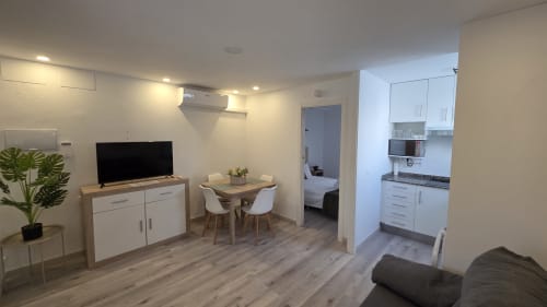 Moderno estudio en Benicàssim con cocina americana, zona de comedor, TV y vista del dormitorio a través de la puerta abierta