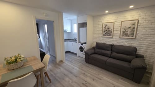 Salón moderno con sofá oscuro, mesa de comedor, pared de ladrillo blanco y entrada a la cocina en Siesta 7, Oropesa